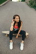 © bodnarphoto - Beautiful girl sits on a skateboard and looks into the camera, wears stylish casual clothes and sneakers, poses on the background of asphalt, top view, street cocnept.