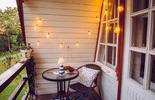 Cute Retro Wooden Nautical Style Balcony View With Small Garden Table And Chair And Decorative String Party Bulbs Lights On In The Evening. 