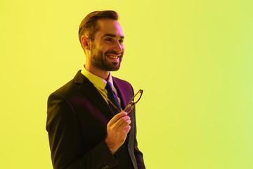 Poster - Cheery smiling happy young business man posing isolated over light green background wall with led neon lights.