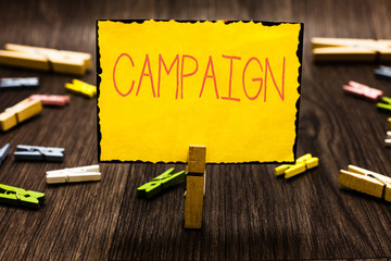 Poster - Handwriting text Campaign. Concept meaning organized course of action to promote and sell product service Clothespin holding yellow paper note several clothespins wooden floor
