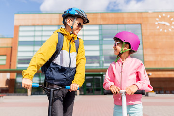 Sticker - education, childhood and people concept - happy school children in helmets with backpacks riding scooters outdoors