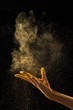 © Yaroslav Danylchenko/Stocksy - Woman's hand scatters gold dust on a black background with copy space. Creative photo for your ideas