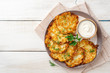Potato pancakes or latkes or draniki with sour cream in plate on white wooden table. Top view. Copy space.