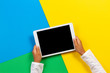 Kid hands with tablet computer on yellow, blue and green background