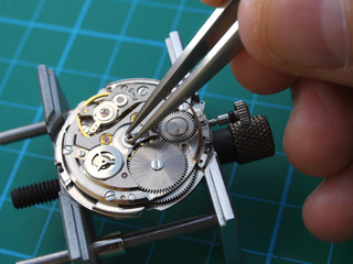 watchmaker repairing old watch mechanism, taking small piece with tweezers