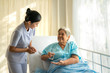 Asian nurse giving medication and glass of water to senior woman at hospital ward. Medicine, age, health care and people concept
