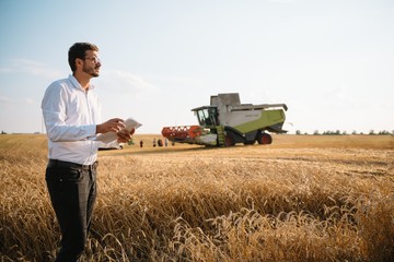 Happy farmer in the field checking corn plants during a sunny summer day, agriculture and food production concept