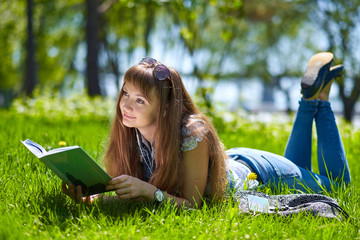 teenage student girl reading a book in park and lying on grass