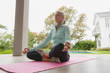 Active senior woman doing yoga on exercise mat in the porch at home