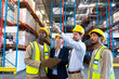 Male supervisor standing with coworkers and pointing at distance in warehouse