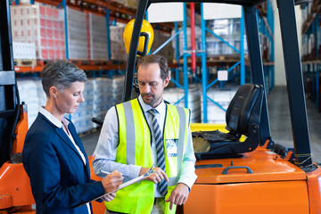 Wall Mural - Male and female staff discussing over clipboard near forklift