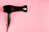 Black hair dryer on pink background composition.