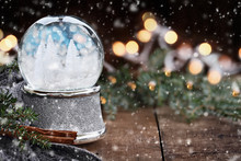 Rustic Image Of A Generic Snow Globe Surrounded By Pine Branches, Cinnamon Sticks And A Warm Gray Scarf With Falling Snow. Blurred With Selective Focus On Snowglobe.