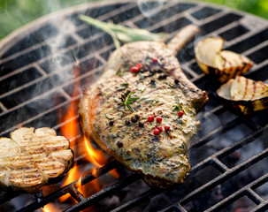 Grilled bone-in pork chop, pork steak, tomahawk in a herb marinade on a flaming grill, close-up.  Barbecue, bbq meat