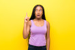 © luismolinero - African American teenager girl with long braided hair over isolated yellow wall thinking an idea pointing the finger up