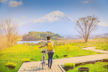 Mountai Fuji With Snow And Flower Garden Along The Wooden Bridge At Kawaguchiko Lake In Japan, Mt Fuji Is One Of Famous Place In Japan. A Women Take A Bicycle On Wooden Bridge.
