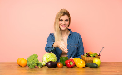 Wall Mural - Young blonde woman with many vegetables shaking hands for closing a good deal