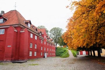 Poster - Copenhagen, Denmark - Red military barracks are separated from a row of trees by a cobblestone road.