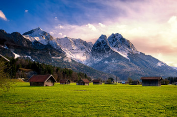 Huts in field at base of Bavarian Alps with snow at sunset