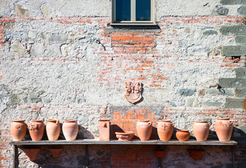 Poster - Castelnuovo di Garfagnana, Tuscany, Italy - A long shelf attached to the outside of an Old World building. The shelf is holding terra cotta pottery.