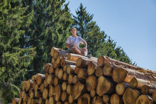 A Man Is Sitting On A Huge Pile Of Wood.