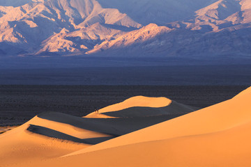 Canvas Print - Hikers walk during sunrise along the ridgeline of a sand dune in the Mesquite Dunes complex inside Death Valley National Park.