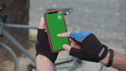 Top view sociable man cyclist riding a bike in the city using modern mobile device green chromakey smartphone screen outdoors. Close-up. People and technology.