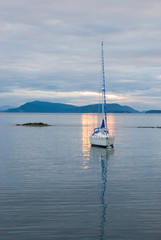 Wall Mural - USA, WA, San Juan Islands. Shaft of setting sunlight through clouds spotlights moored sailboat