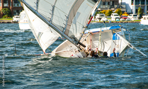 Two children in the water climbing back into a capsized sailboat.