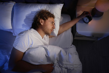 Sticker - Sleepy young man turning off alarm clock on nightstand, view from above. Bedtime