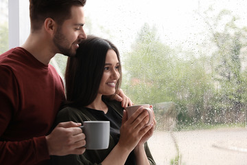 Canvas Print - Happy young couple near window indoors on rainy day