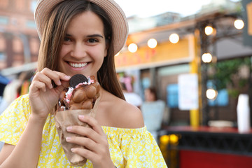 Wall Mural - Pretty young woman holding delicious sweet bubble waffle with ice cream outdoors