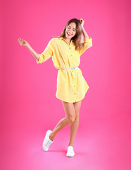 Canvas Print - Beautiful young woman in yellow dress dancing on pink background