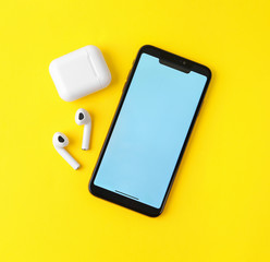 Wireless earphones, mobile phone and charging case on yellow background, flat lay. Space for text