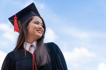 Asian graduate woman in cap gown on blue sky background.