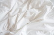 Closeup of beautiful white shiny crumpled polyester fabric sheets on the bed with warm motion and feeling for background and decoration. Cloth washing and laundry concept at home