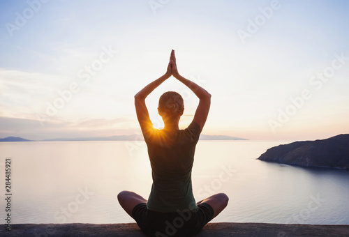 Fotomural Young woman practicing yoga near the sea at sunset