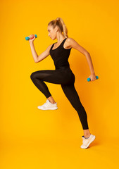 Poster - Young Woman Exercising Jumping With Dumbbells On Yellow Studio Background