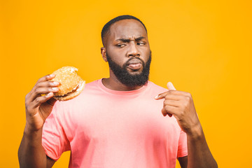 Young african american man eating hamburger isolated over yellow background.