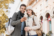 © kite_rin - Beautiful happy couple using smartphone. Young joyful smiling woman and man looking at mobile phone in a city in autumn.  Technology, travel, tourism, students concept