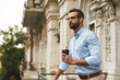 © Friends Stock - Young and handsome bearded man in eyeglasses and formal wear holding cup of coffee and looking away while standing at the office balcony
