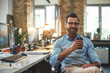 © Friends Stock - I can not work without coffee. Portrait of young bearded man in eyeglasses and headphones holding cup of coffee and smiling at camera while sitting in the modern office