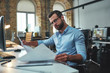 © Friends Stock - Construction concept. Concentrated bearded engineer in eyeglasses and formal wear looking at blueprint while working in the office