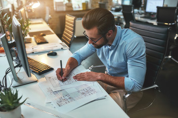 Architectural project. Successful busy bearded man in eyeglasses and formal wear drawing something while working in the office