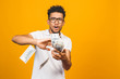 © denis_vermenko - Portrait of a happy young afro american man throwing out money banknotes isolated over yellow background.