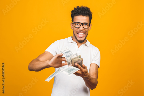 Fotografía Portrait of a happy young afro american man throwing out money banknotes isolated over yellow background
