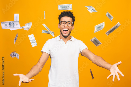 Cuadros en Lienzo Portrait of a happy young afro american man throwing out money banknotes isolated over yellow background