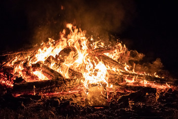 Campfire at night, with its soothing flickering flames and red and orange glow of the burning logs at dark night