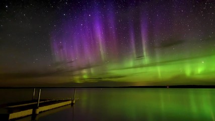 time lapse of vivid aurora (northern lights) over a calm reflecting lake with a dock in the foregrou