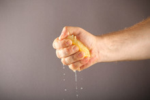 Lemon Pressed By Hand Against A Plain Background